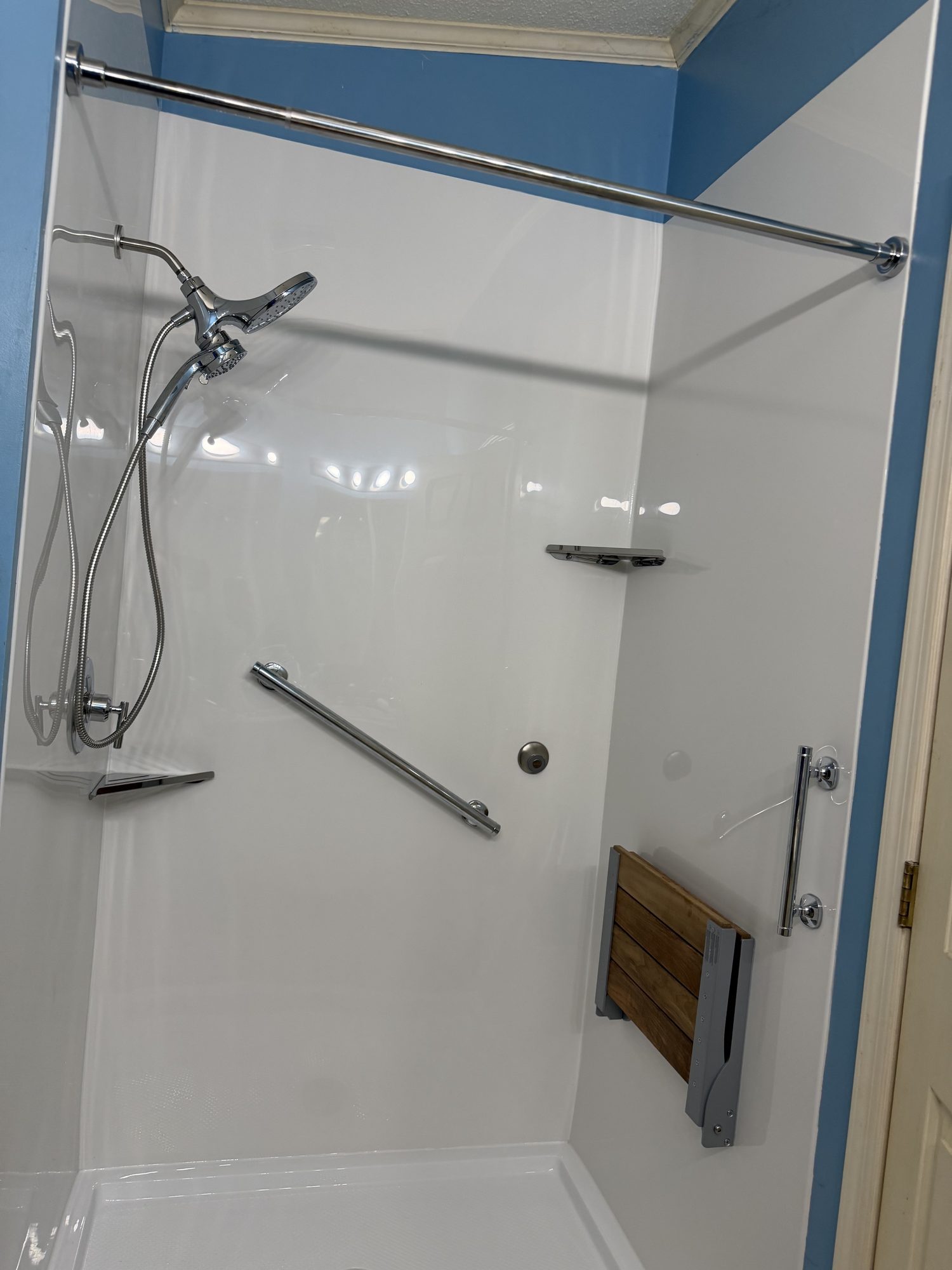 A Carolina Bath Solutions walk-in shower with grab bars, a handheld sprayer and a fold-down teak seat