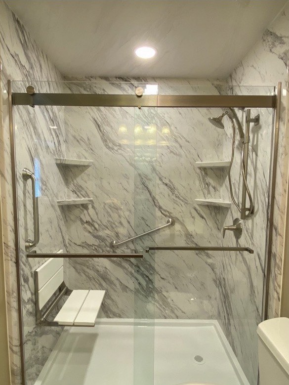 A finished Carolina Bath Solutions walk-in shower with marble-look acrylic panels, grab bars and a fold-down seat